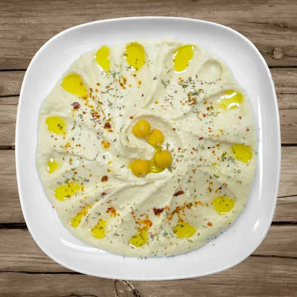 Creamy hummus drizzled with olive oil, herbs, and whole chickpeas on a white plate.