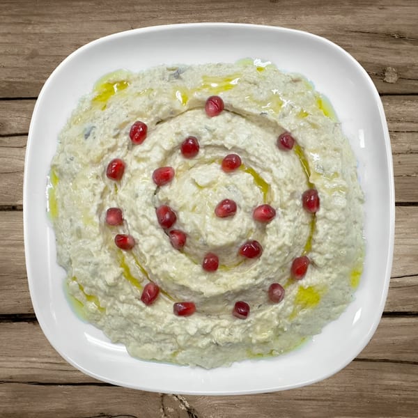 Creamy Mediterranean dip, possibly baba ghanoush, garnished with pomegranate seeds and olive oil.