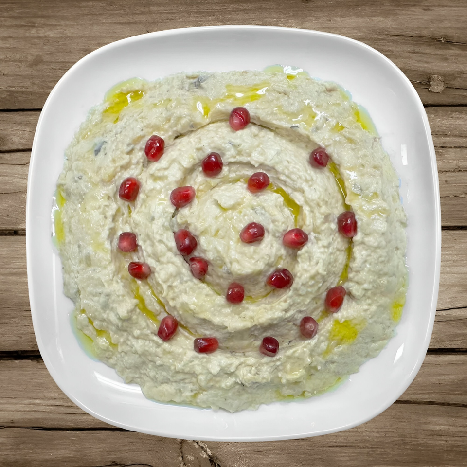 Creamy Mediterranean dip, possibly baba ghanoush, garnished with pomegranate seeds and olive oil.