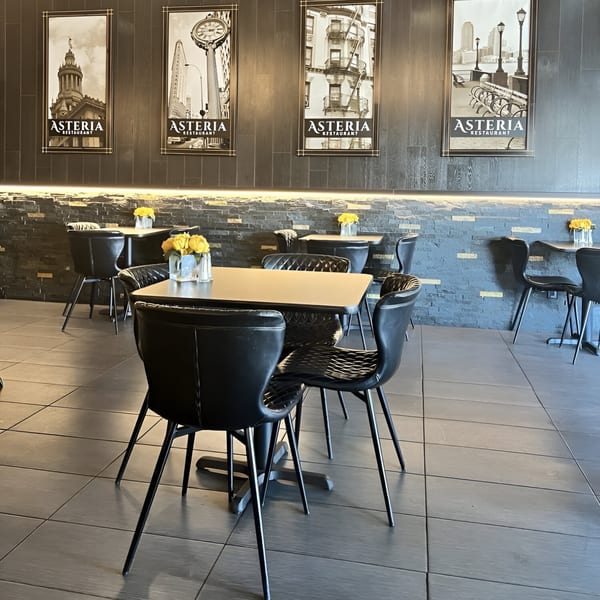 Interior of Asteria Restaurant with black tables and chairs, and cityscape art on dark wood walls.