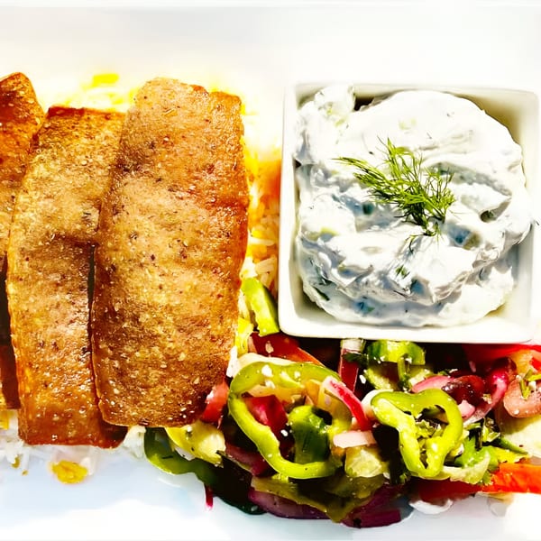 Asteria Restaurant's Mediterranean dish with golden-brown fish, rice, fresh salad, and tzatziki sauce.